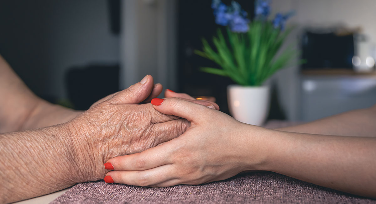 A carer holds the hand of an elderly woman with Parkinson's disease.