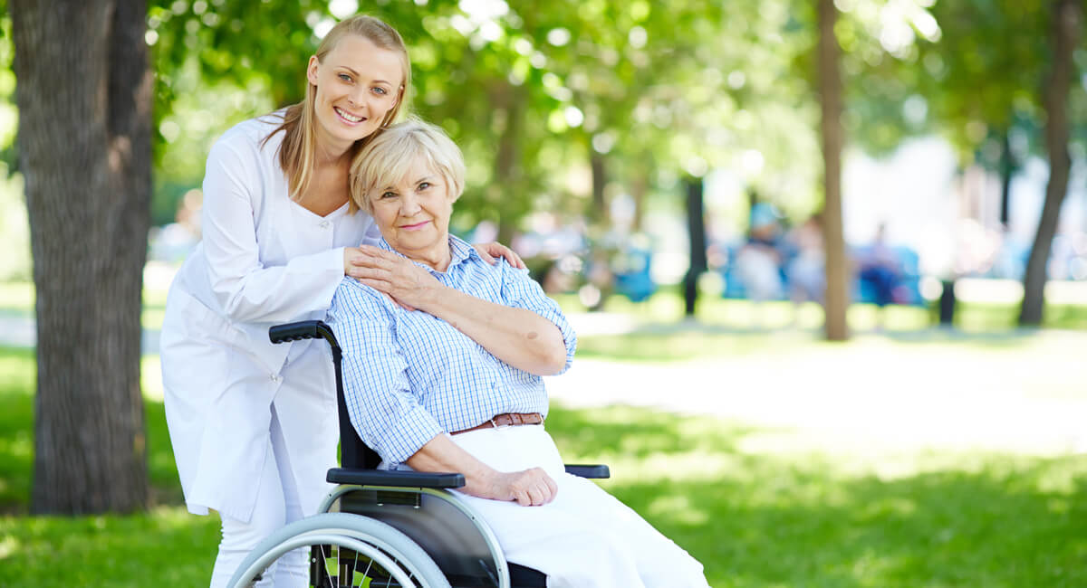 A carer in a garden posing for a photo with a senior woman in a wheelchair.