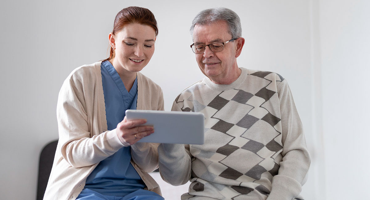 An agency homecare worker assisting an elderly man with using a notepad.