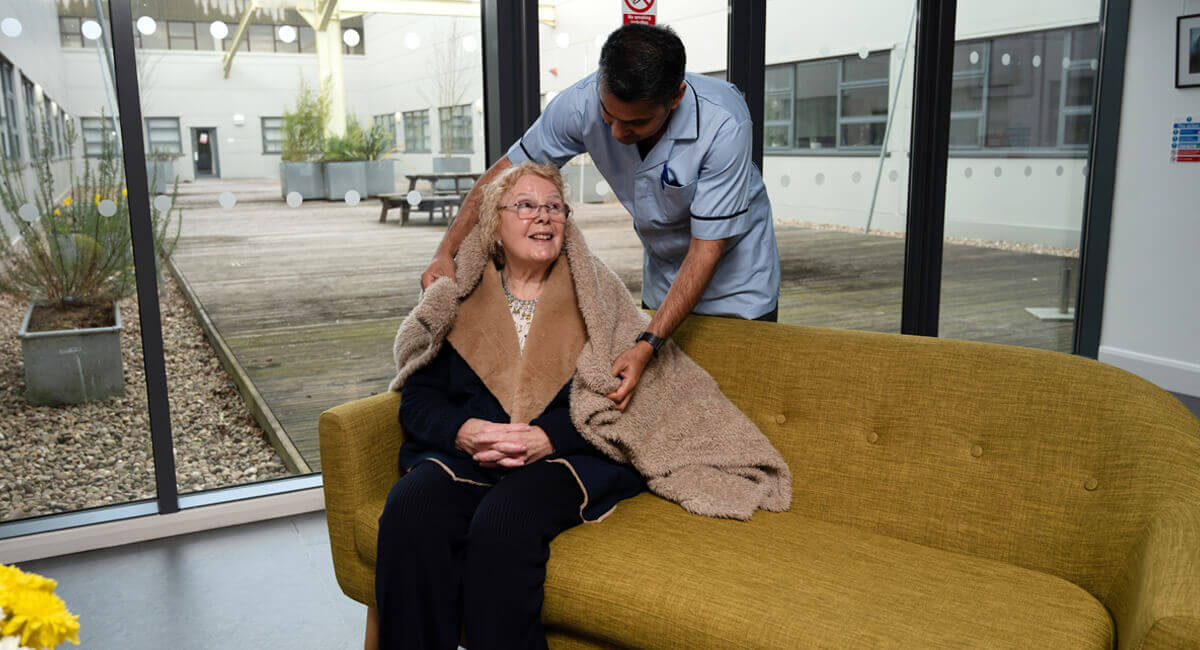 Due to the cold weather, a care assistant wraps a blanket around a senior.