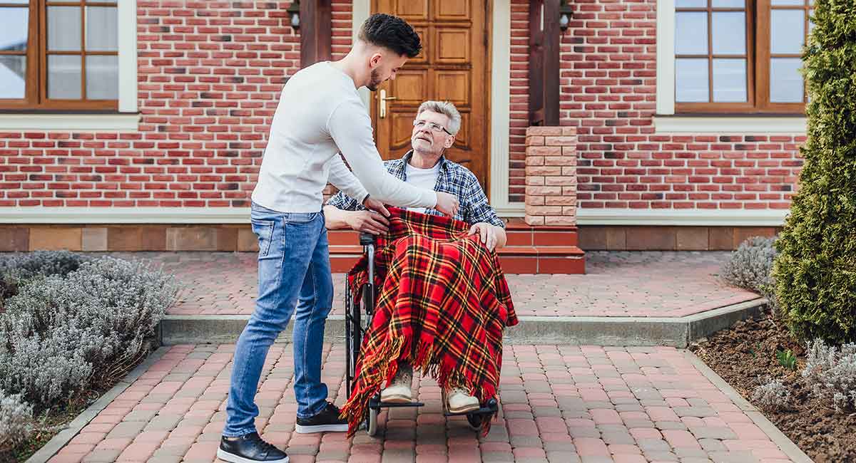 A carer covers a blanket over the wheelchair-bound patient's thighs.