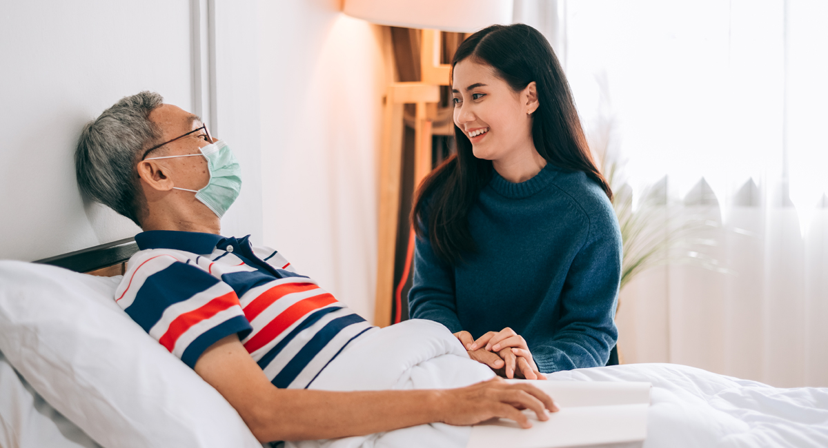 A carer providing person-centred care to an elderly man who is bedridden.